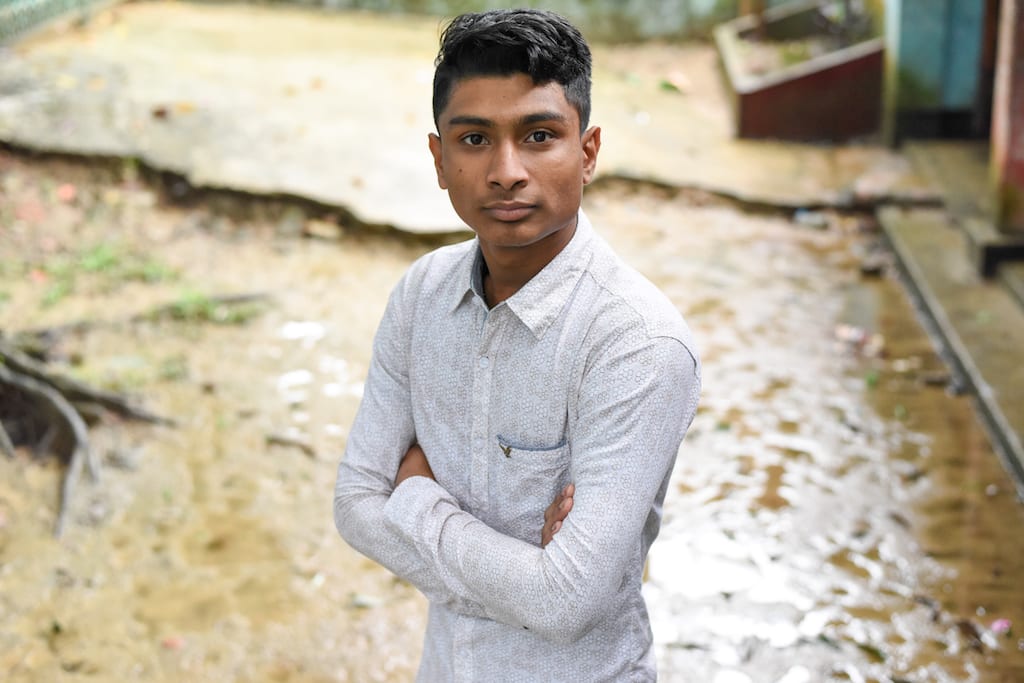 Teenage boy wearing a white button up shirt crosses his arms and looks at the camera.